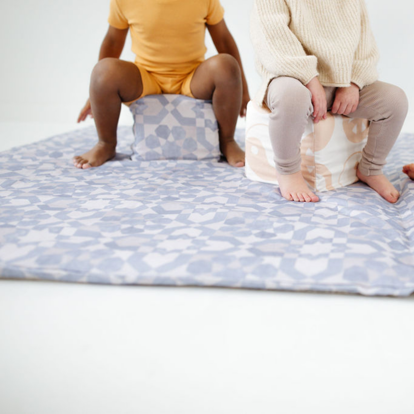 Two children sitting on patterned cushions on a white floor.
