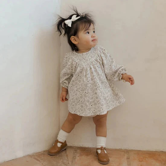 Lifestyle photo of toddler girl in a long sleeve white dress with blue and gray florals.