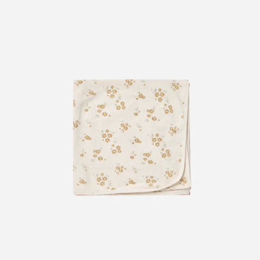 A folded beige baby blanket with a floral pattern, presumably made of organic cotton.
