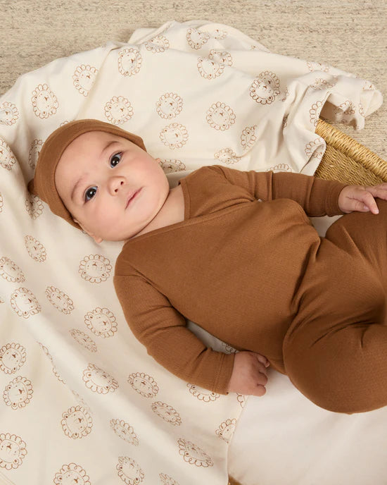A baby wearing a brown pointelle wrap footie with a snap closure on the interior and button closure laying in a basket.