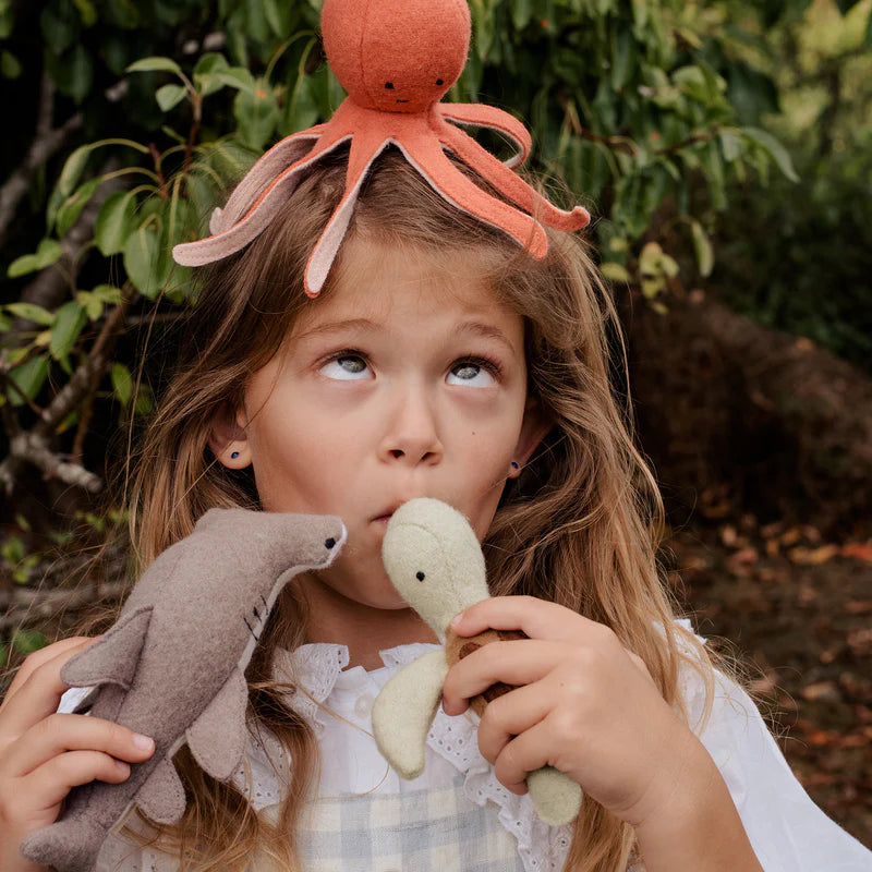 Girl holding three plush toy animals representing marine life - an octopus, a turtle, and a shark, all made from a soft wool blend with embroidered features.  The octopus on her head and the turtle and shark in hand.