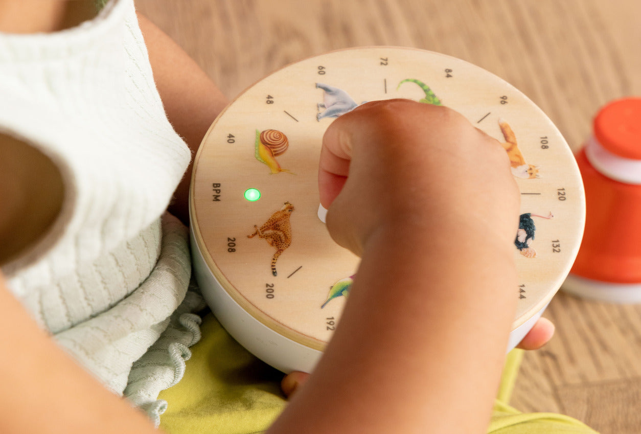 Child's hand interacting with a round, colorful device featuring cartoon characters on a wooden surface.