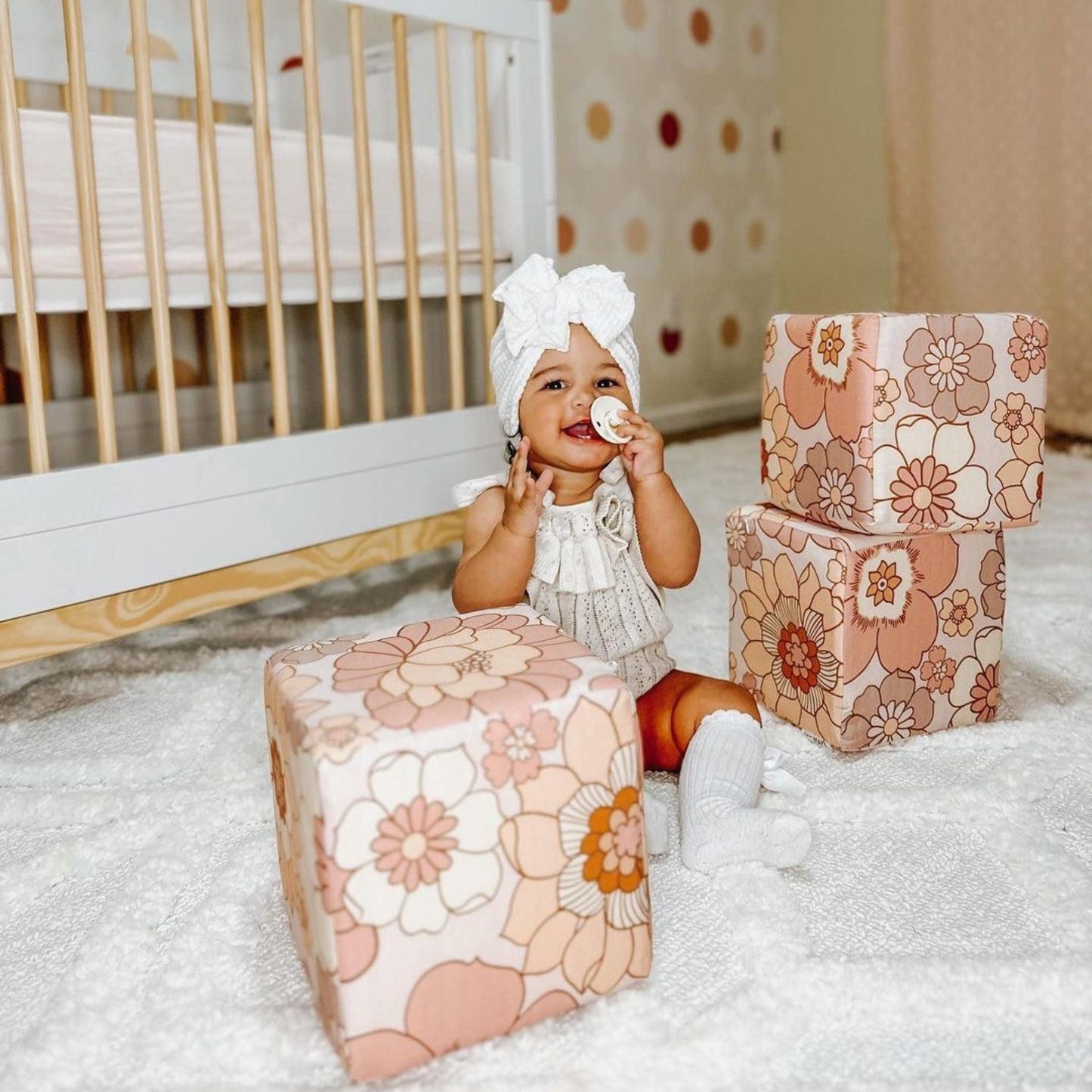 Baby sitting on a bed with floral-patterned boxes in a nursery setting