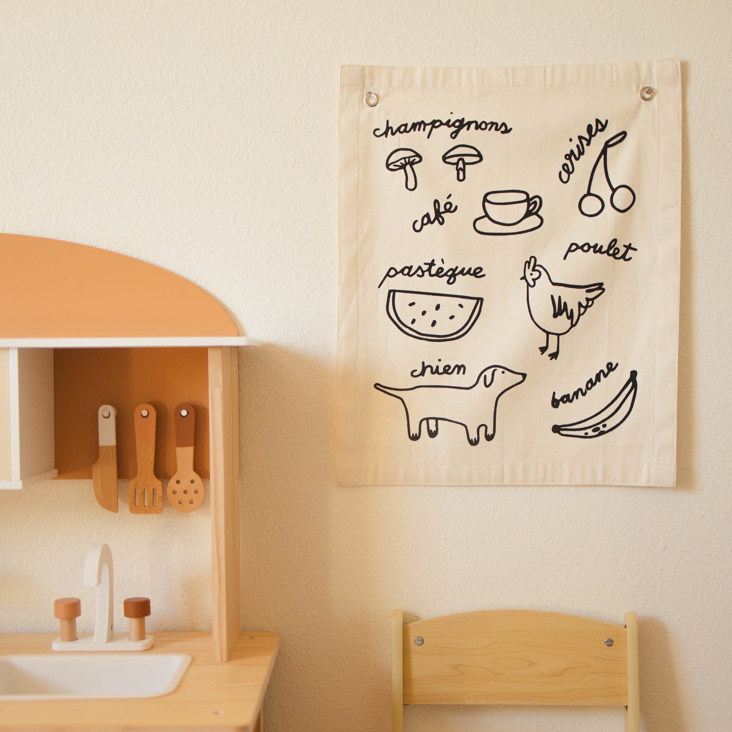 Children's play kitchen with a wall hanging featuring illustrations and text.