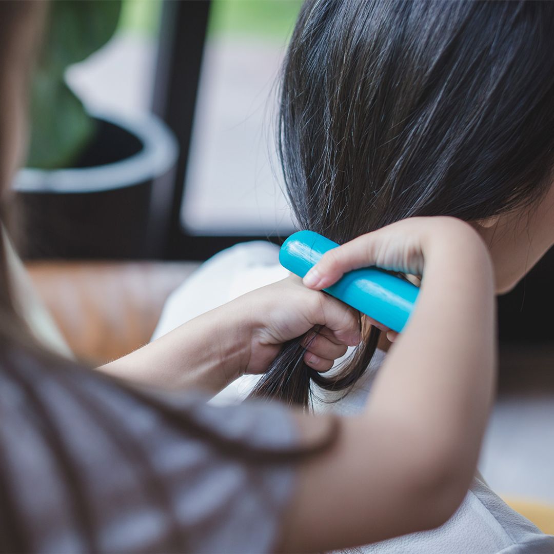 Person styling a child's hair with a blue brush in a home setting