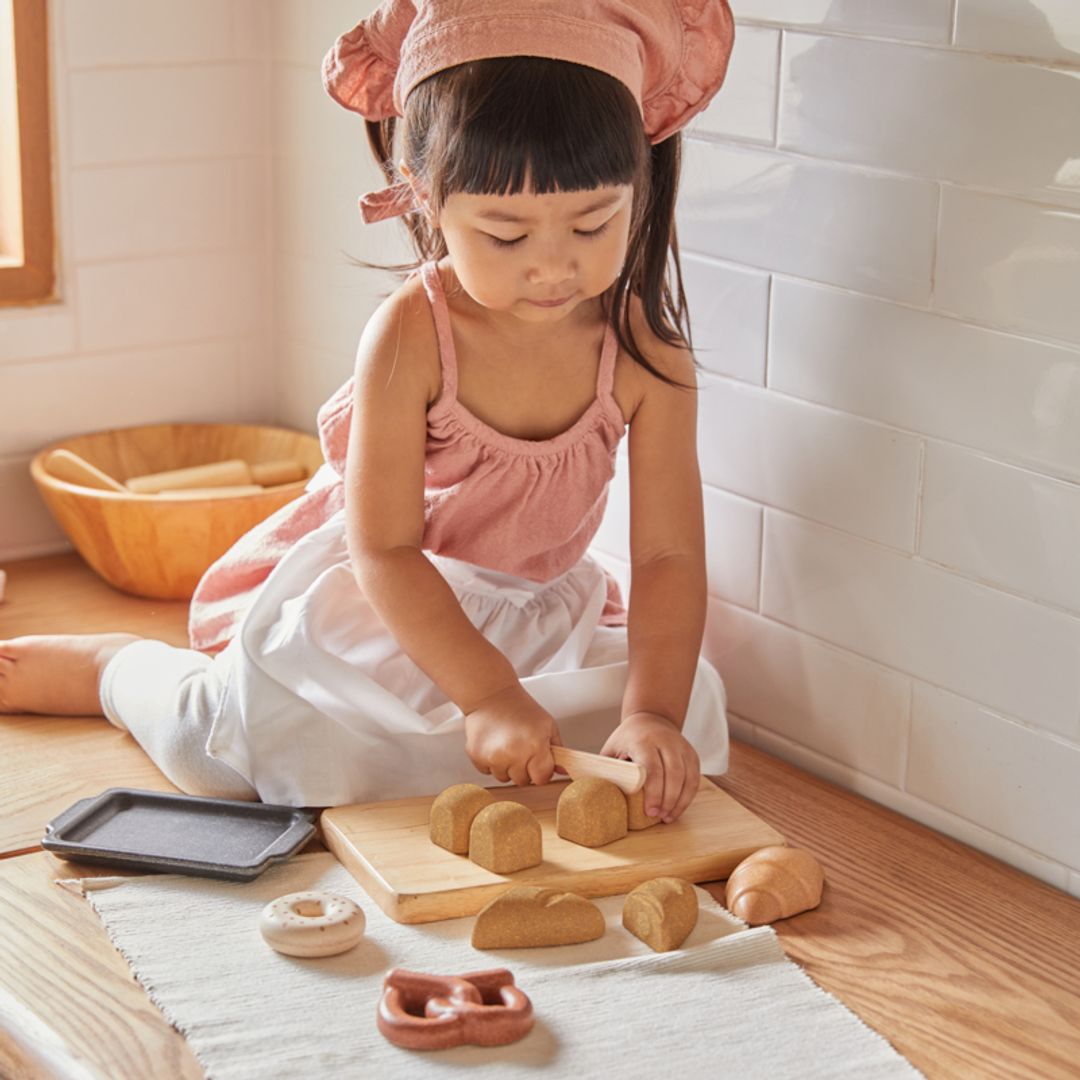 Child playing with wooden play dough and tools on a wooden floor.