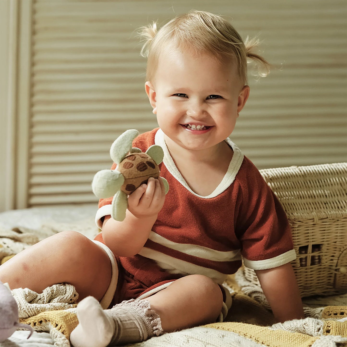 Smiling baby in a brown and white terry cloth shorts set holding a plush turtle.