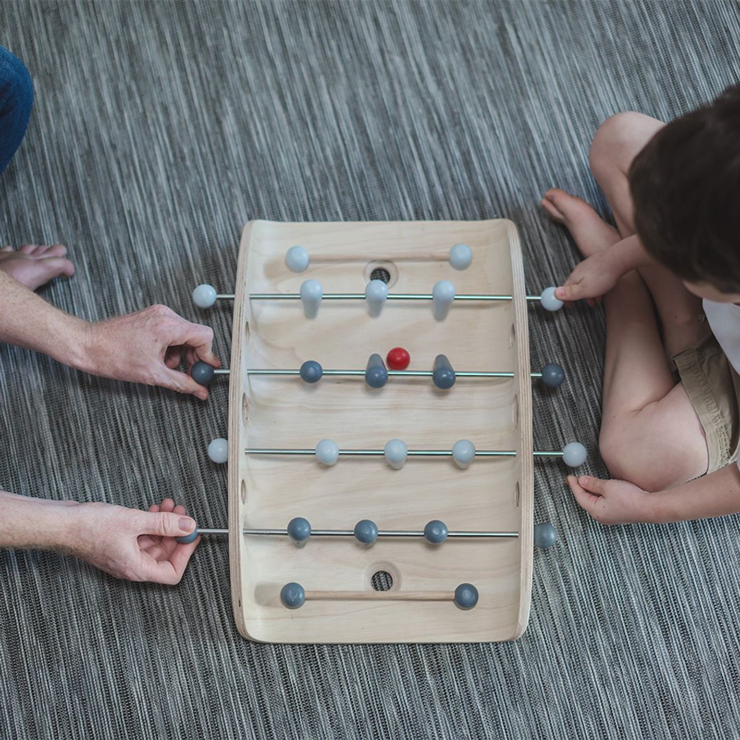 Two people playing with a small wooden foosball table on a gray carpet.