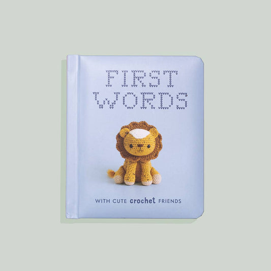 A board book titled 'First Words w/ Cute Crochet Friends' featuring a crochet lion cover design, intended for infants and toddlers.