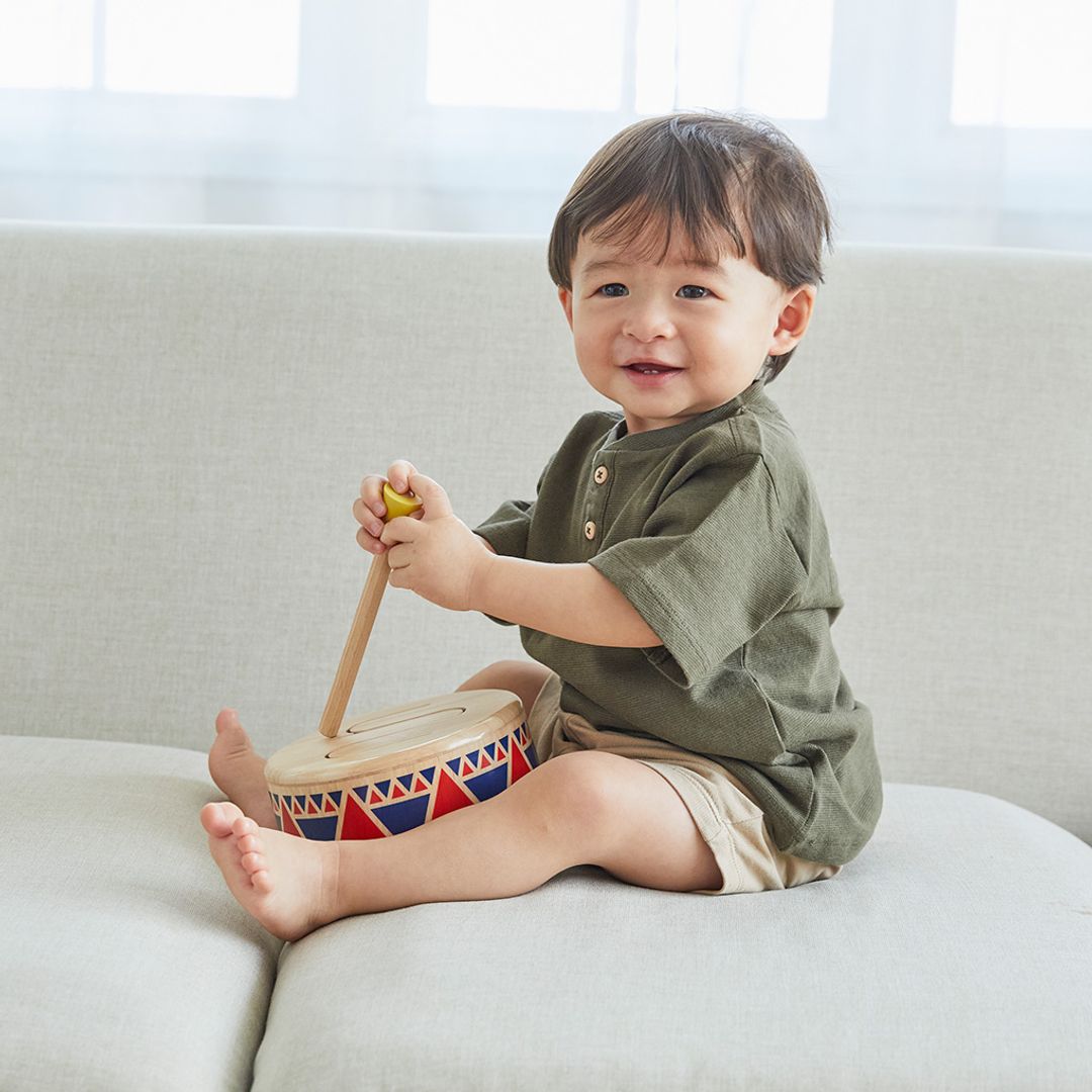 Child playing with a colorful toy drum on a light-colored couch.