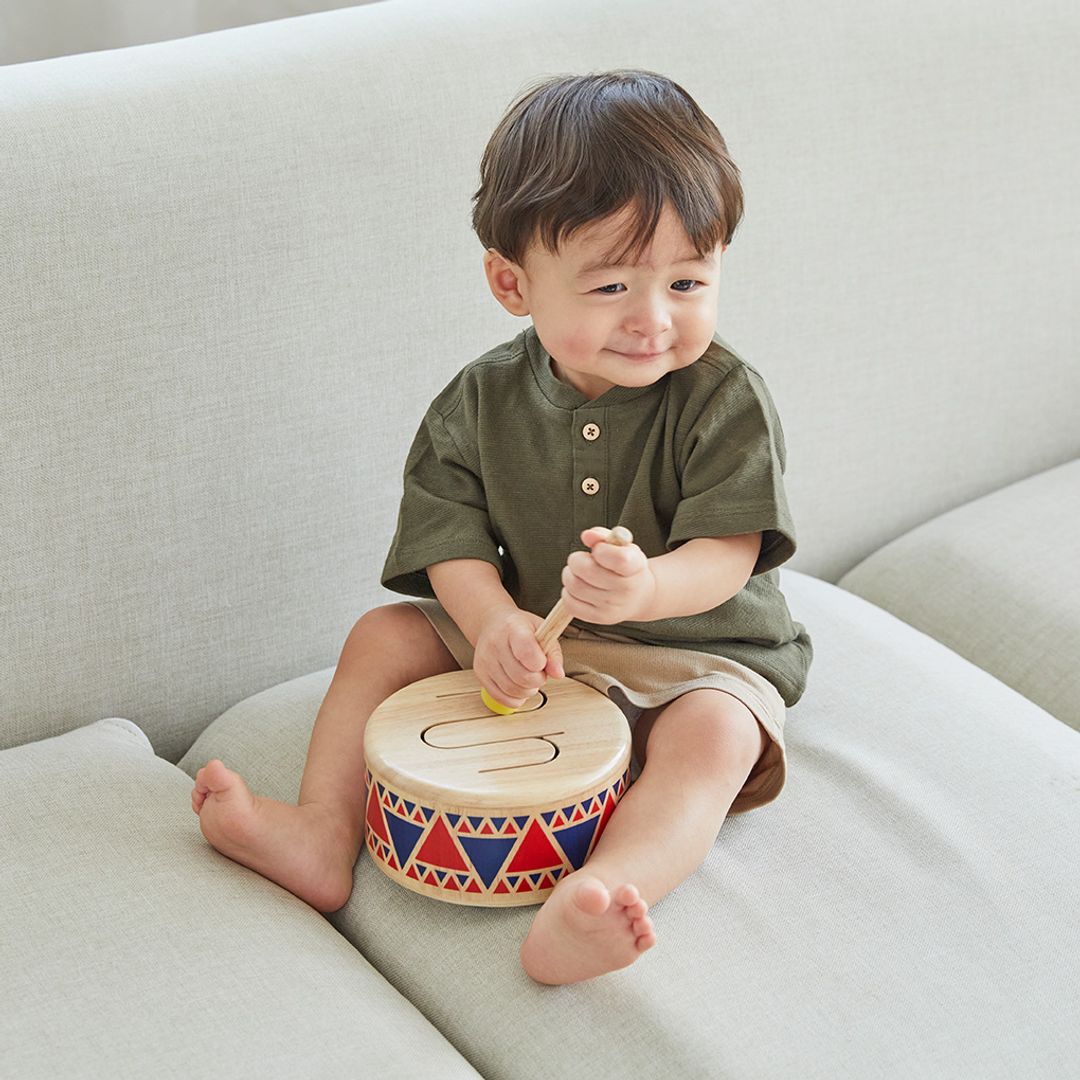 Child playing with a colorful toy drum on a light-colored couch