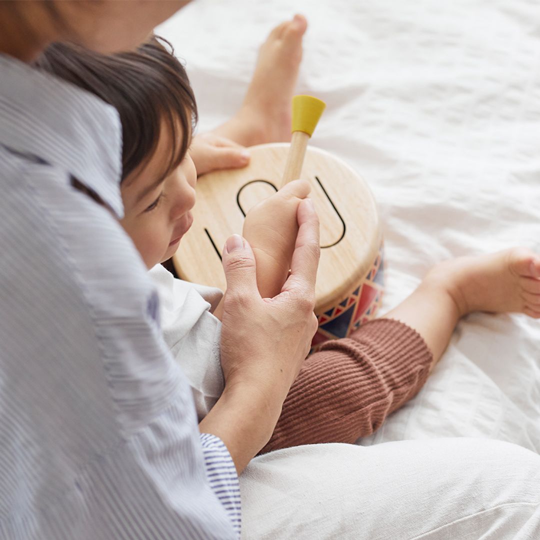 Child playing with a wooden drum toy on a bed