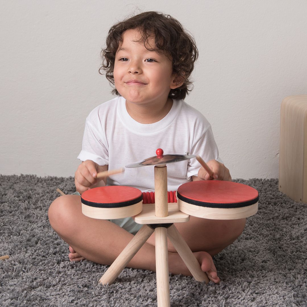 Child playing with a wooden toy drum set on a gray carpet.