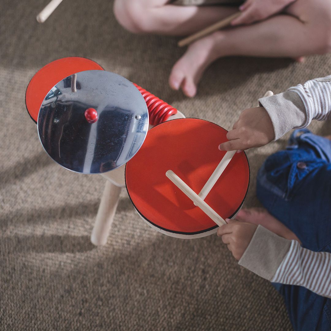 Children playing with a small drum set on a carpeted floor