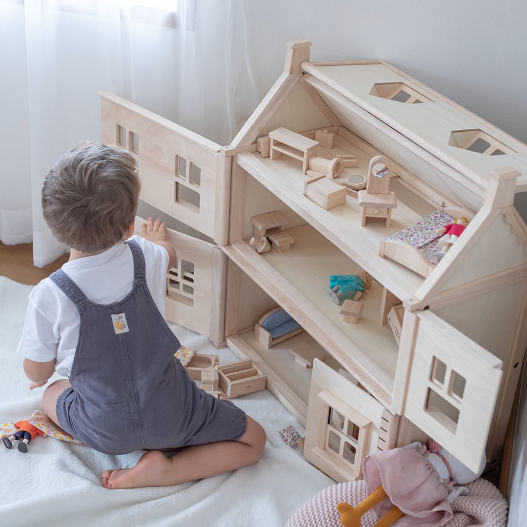 Child playing with a wooden dollhouse and toys on a bed.