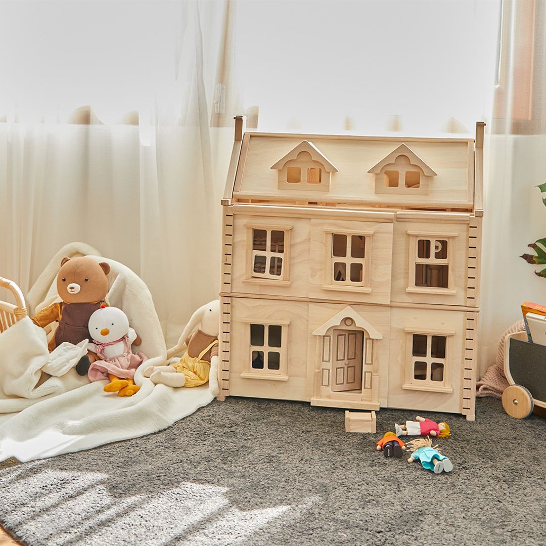 Wooden dollhouse with toys on a carpeted floor in a softly lit room.