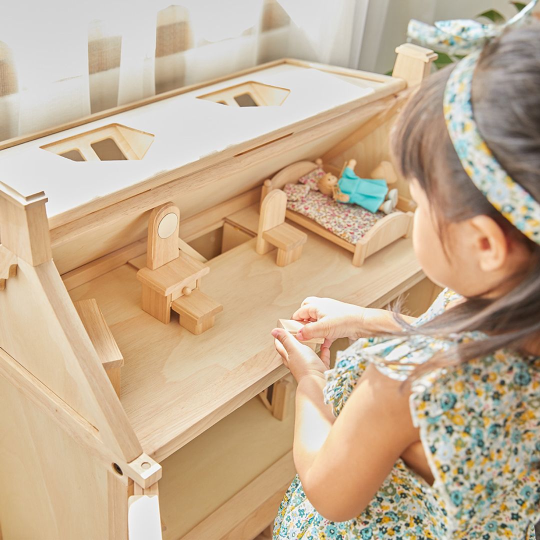Child playing with a wooden dollhouse and dolls.