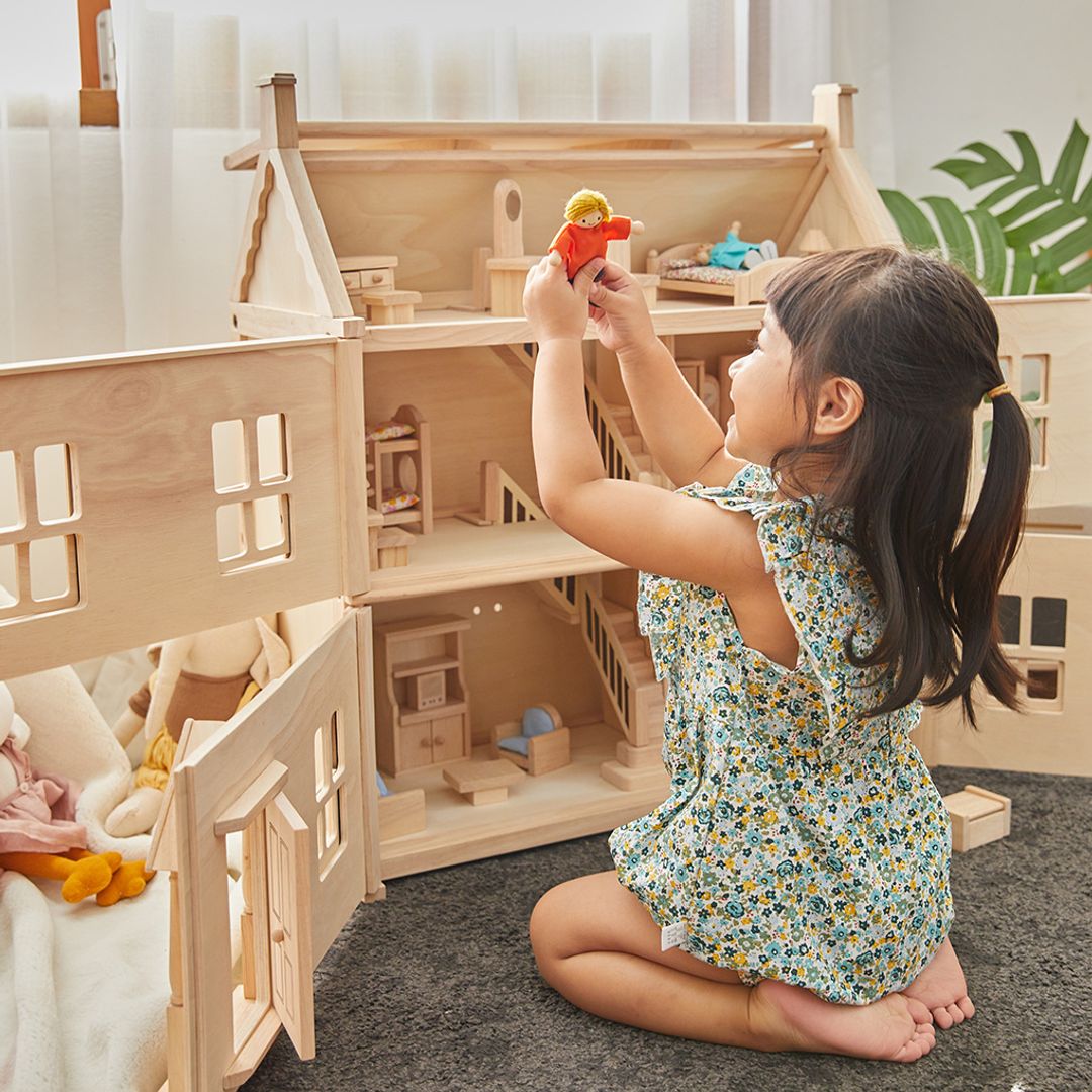Child playing with a wooden dollhouse and toys indoors.