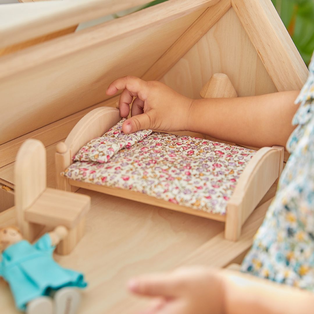 Child playing with a wooden dollhouse and dolls
