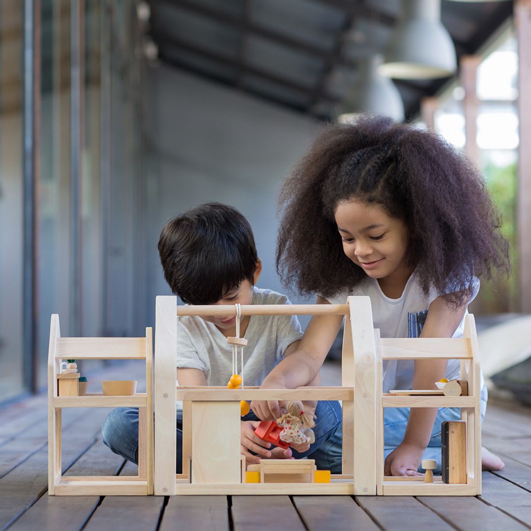 Two children playing with a wooden toy set on a wooden deck.