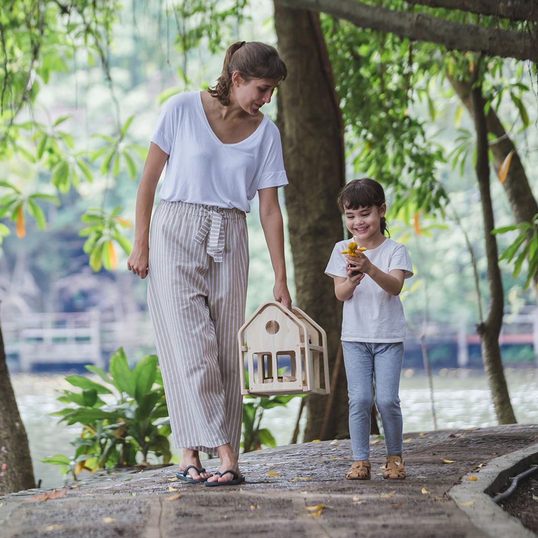 Woman and child standing outdoors with a small wooden house model