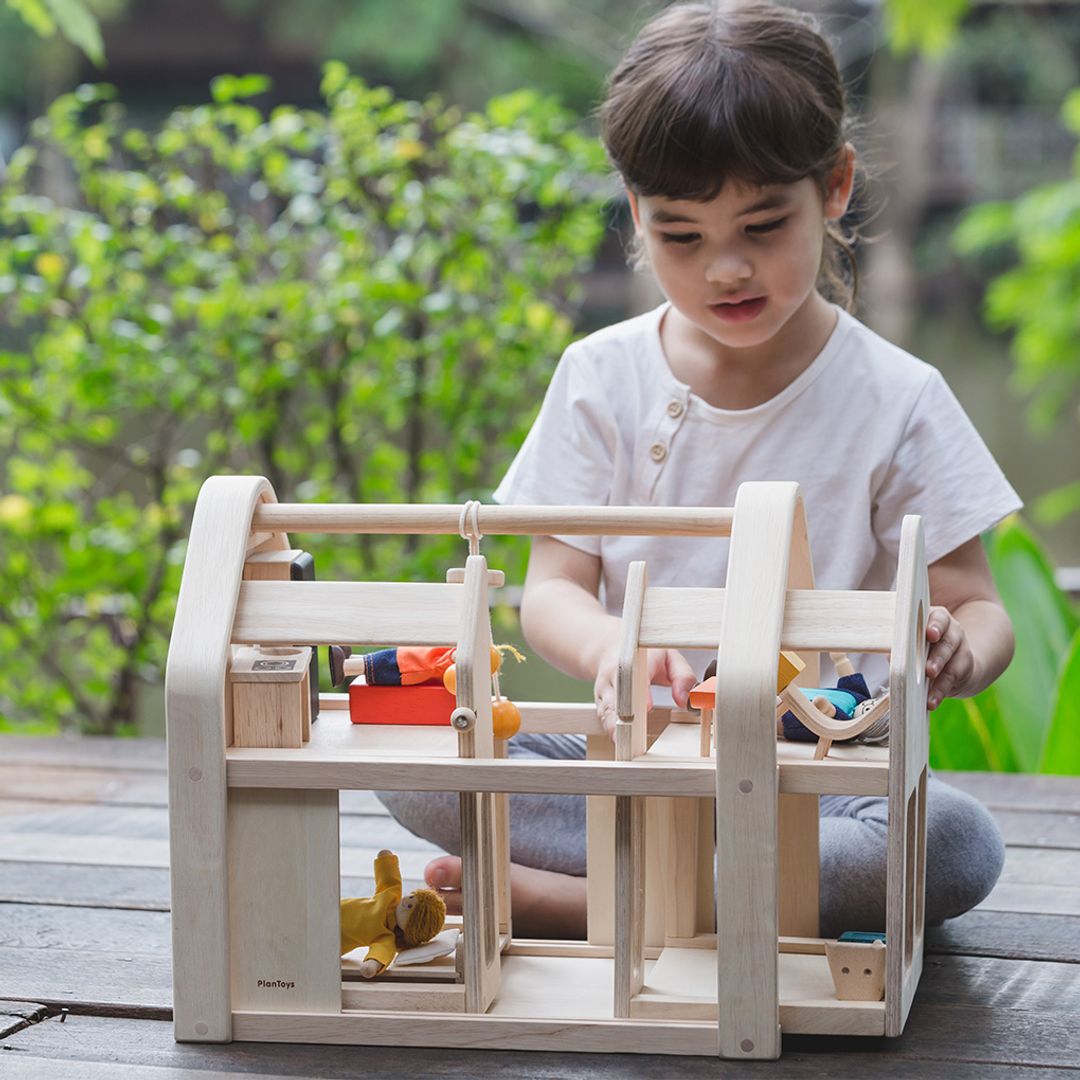 Child playing with a wooden dollhouse outdoors