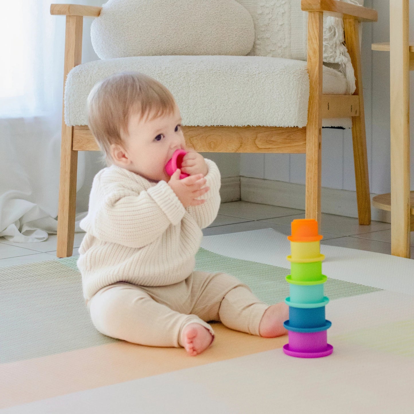 Baby playing with a colorful stack of rings on the floor.