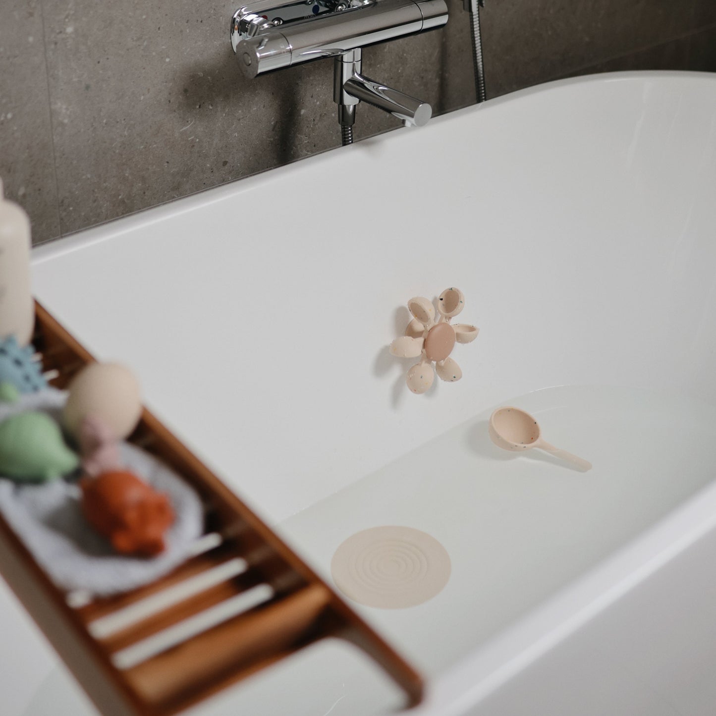 Bath tub with bath toys and a wooden tray in a bathroom setting