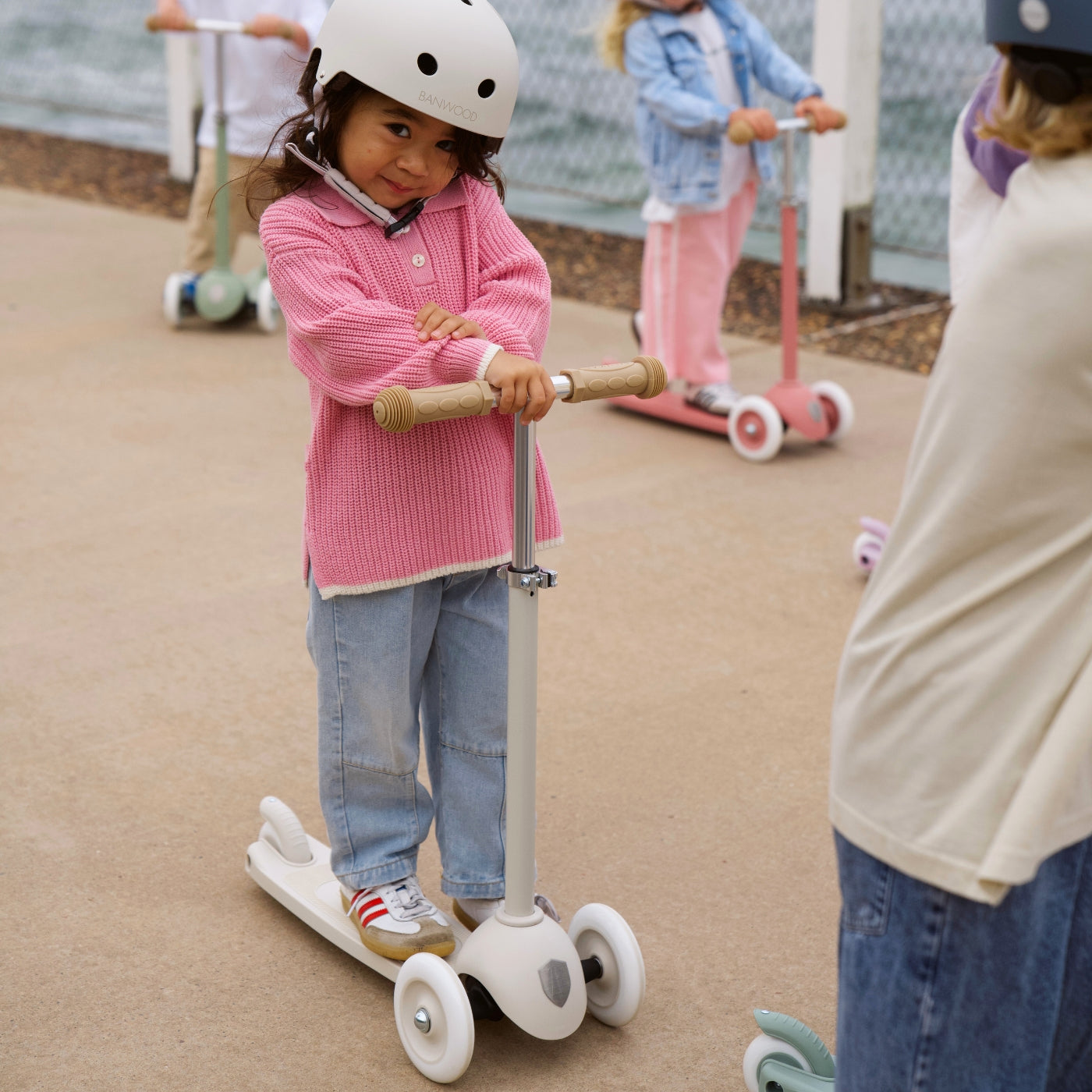 Child on a scooter with a helmet, standing on a playground surface.