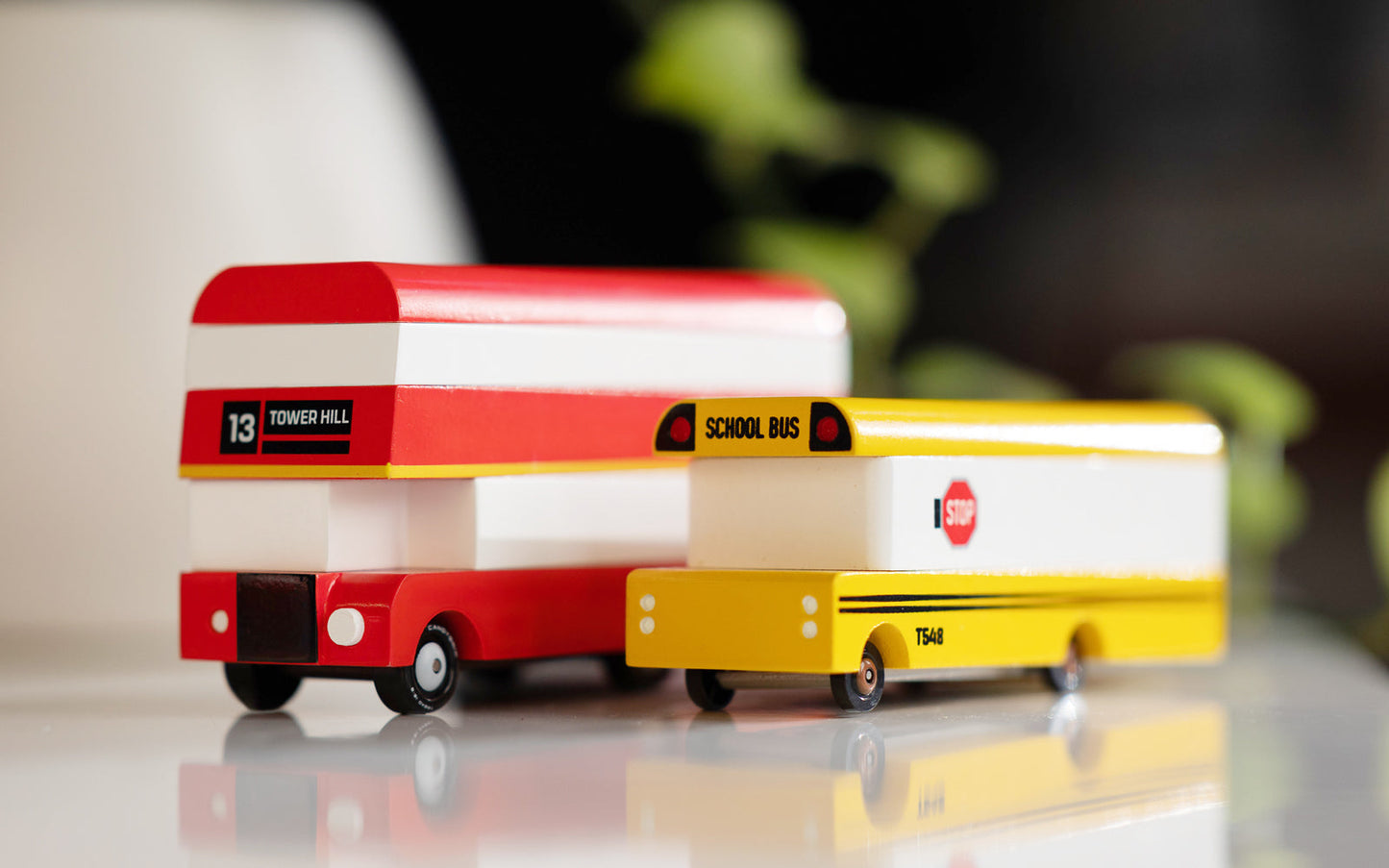 Model of a red and white school bus with a yellow trailer on a reflective surface.