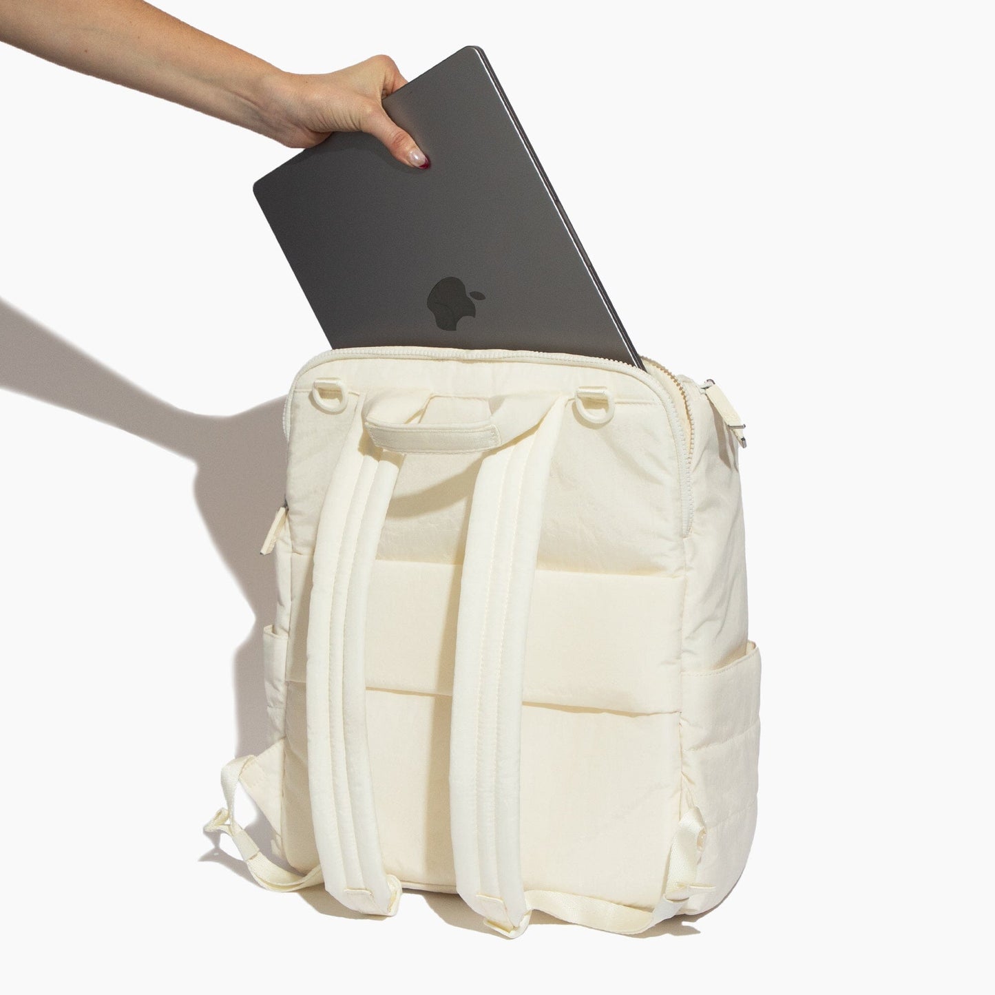 White backpack with a laptop being placed into it on a white background