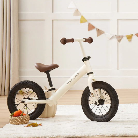 White balance bike with brown handlebars and seat on a light-colored rug.