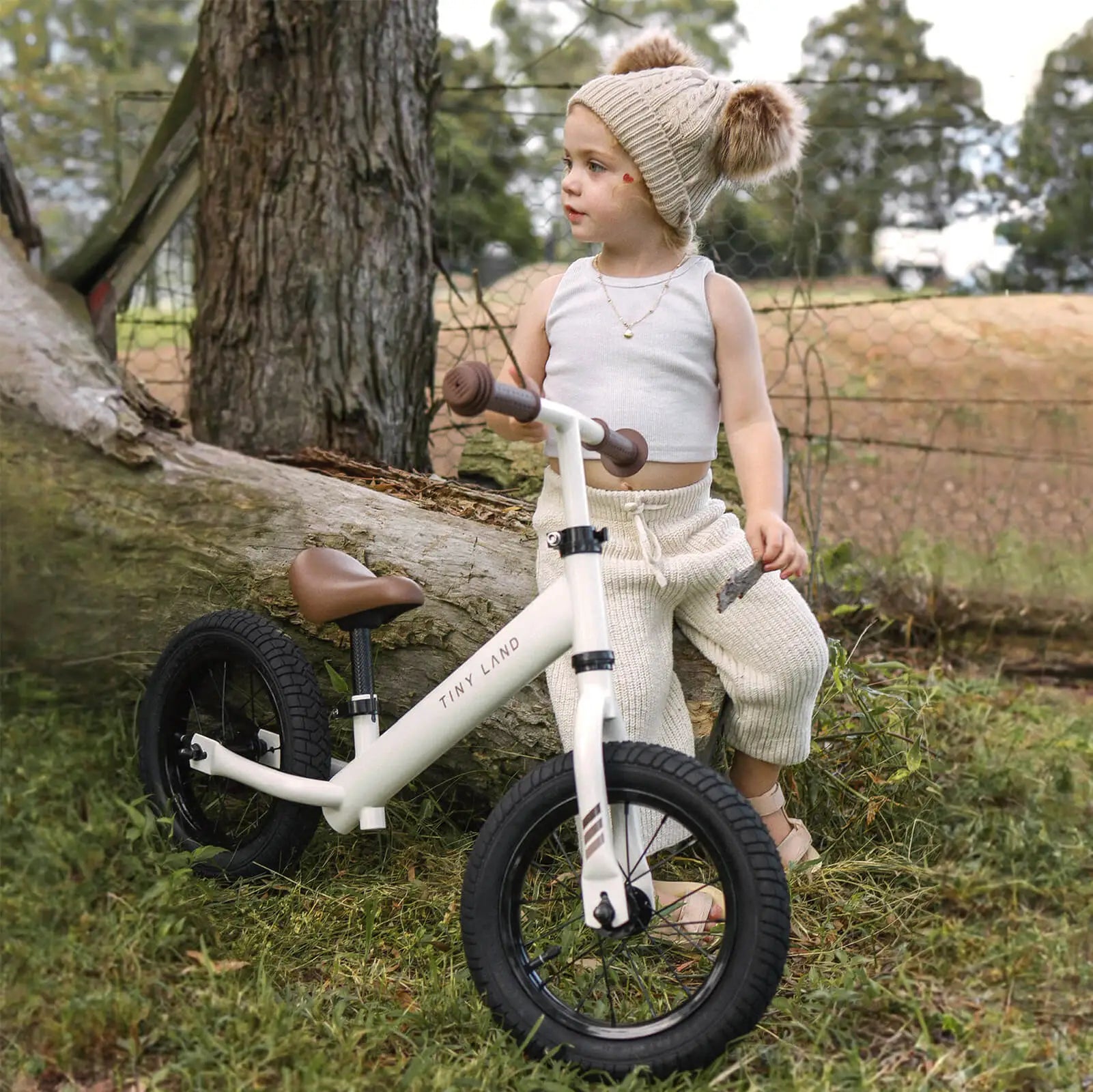 Child sitting on a balance bike in a natural outdoor setting with trees and grass.