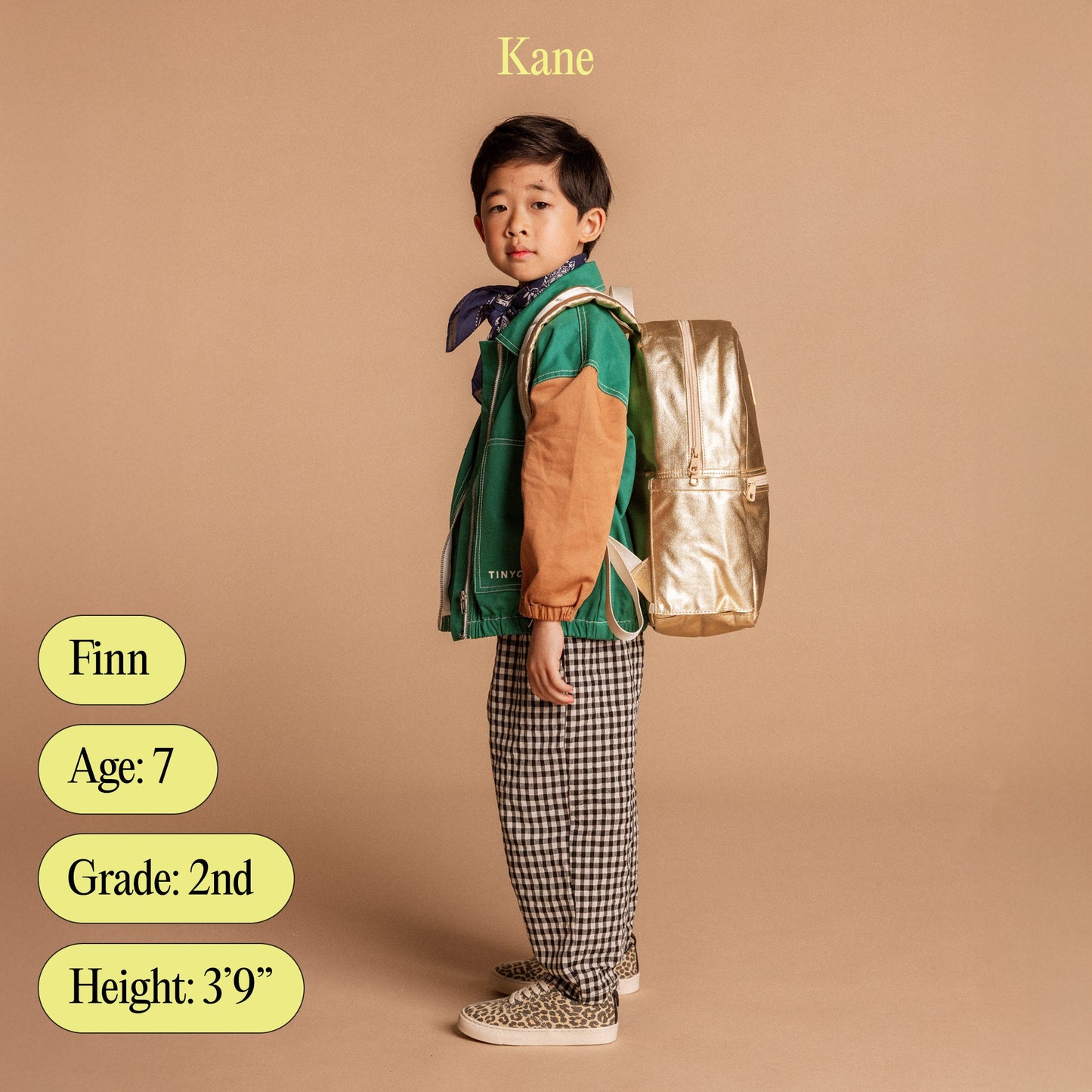 Child wearing a green jacket with a gold backpack on a beige background