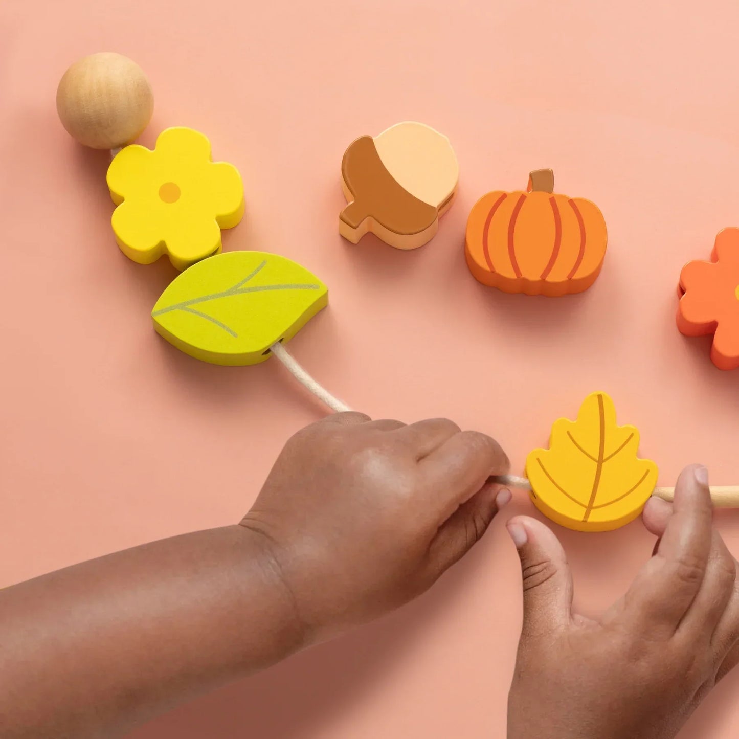 Wooden shape sorter toy with hands interacting on a pink background
