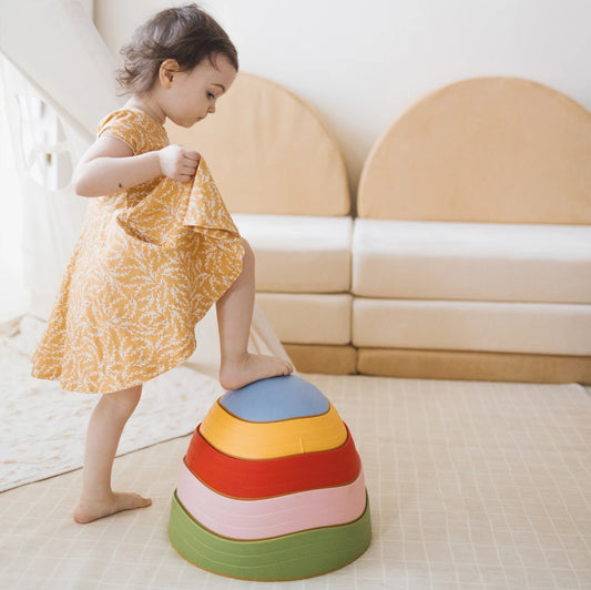 Child in a yellow dress stepping on a colorful stool in a modern living room.