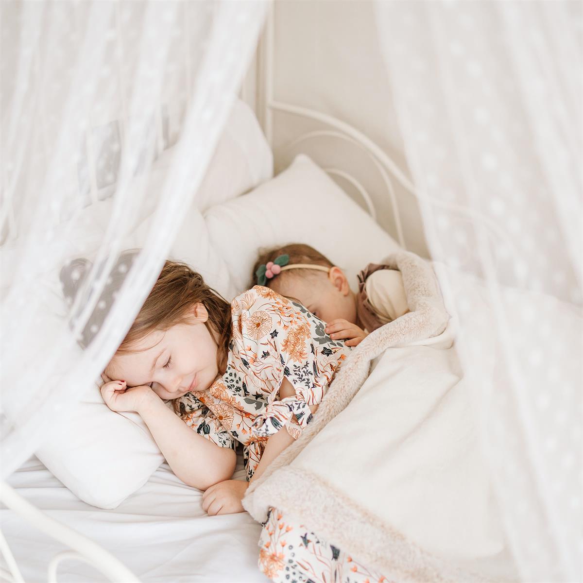 Two children sleeping in a cozy bed with white bedding and a soft blanket.