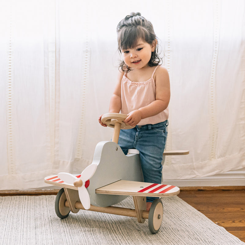 Child playing with a wooden toy airplane indoors