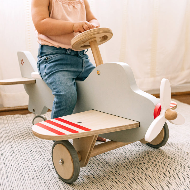 Child playing with a wooden toy airplane on a carpeted floor.