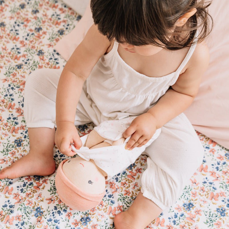 Child playing with a pink toy on a floral blanket