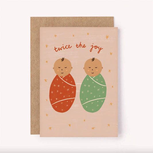 A greeting card with an illustration of two baby feet in red and green onesies, with the text 'Twice the joy' and a star pattern in the background.
