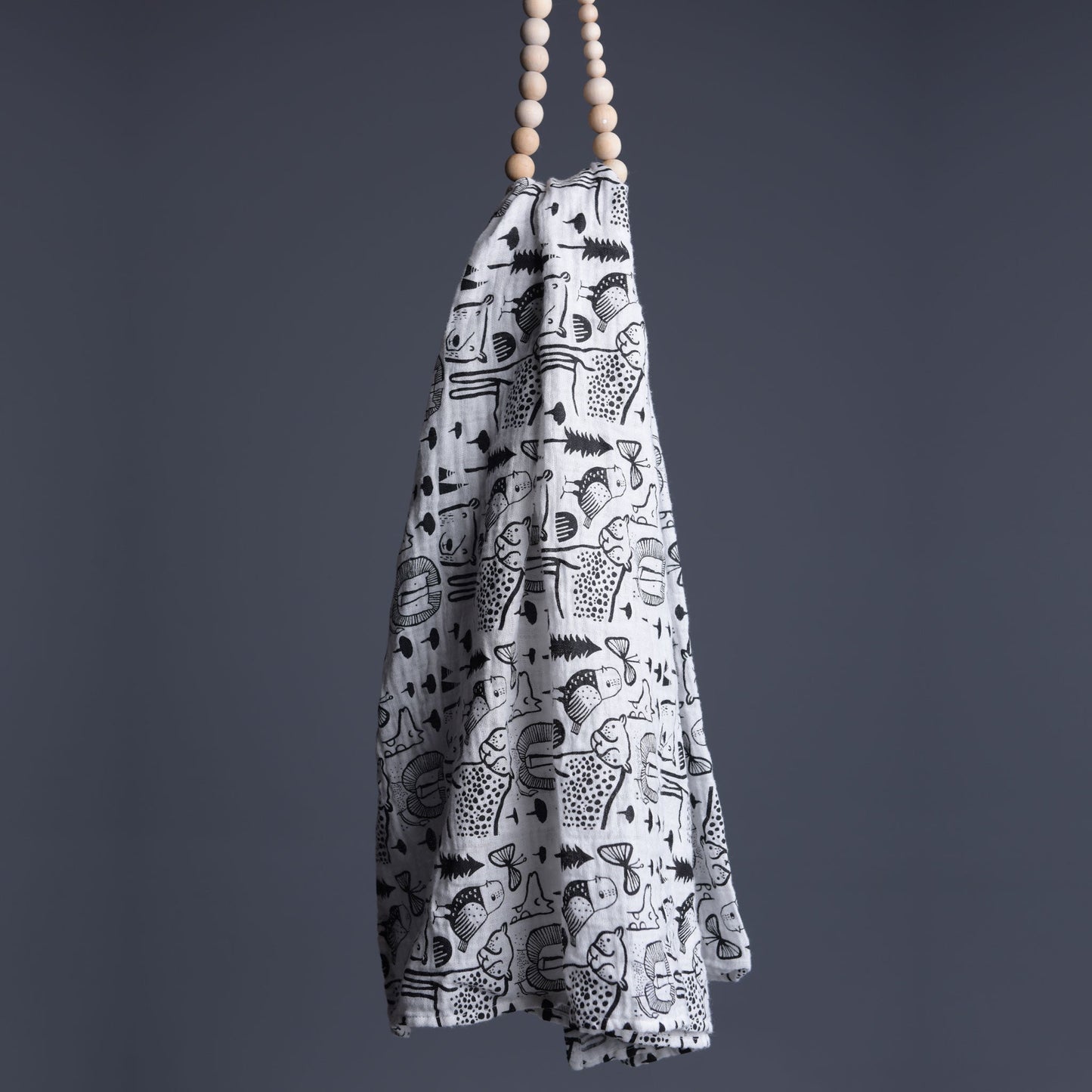 White towel with black patterns hanging from wooden beads against a gray background