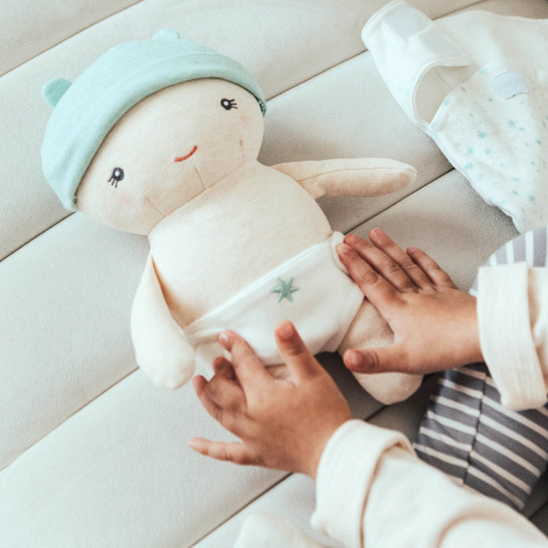 Child's hands holding a plush toy with a light blue hat on a soft surface