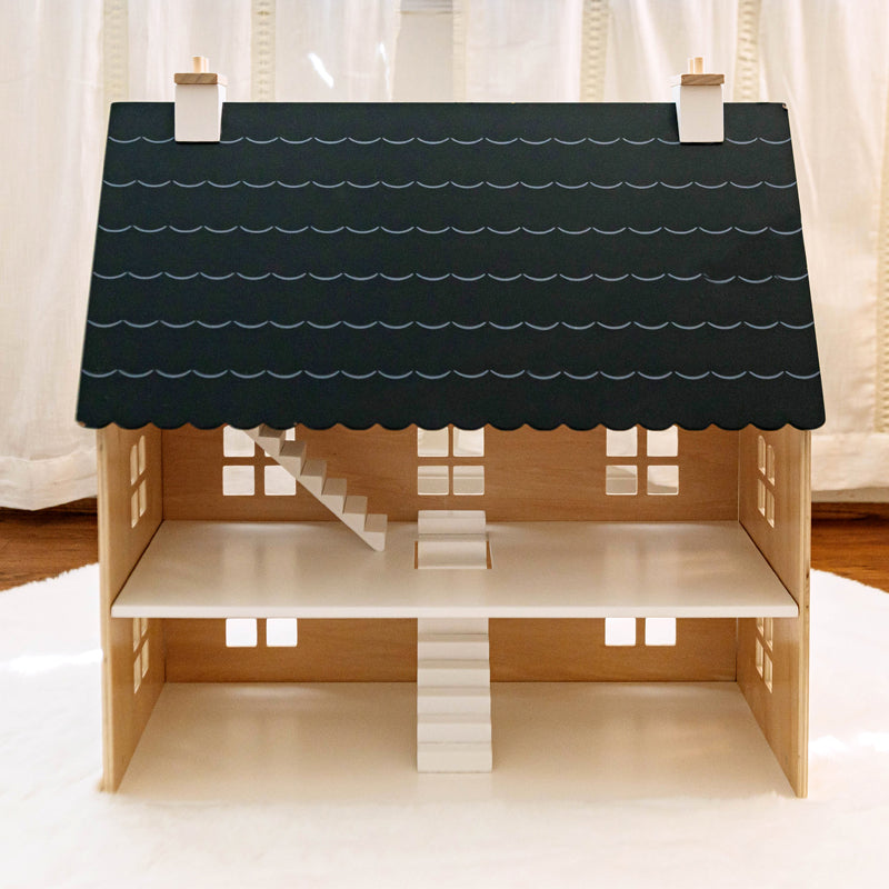 Wooden dollhouse with a black roof against a white curtain background
