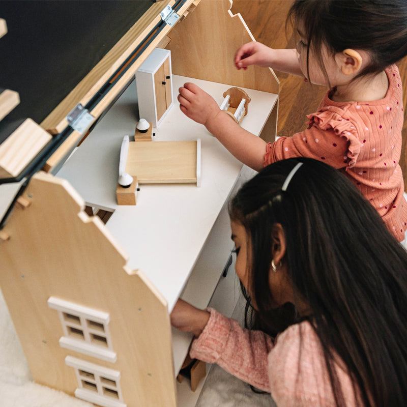 Two children playing with a wooden dollhouse and accessories.