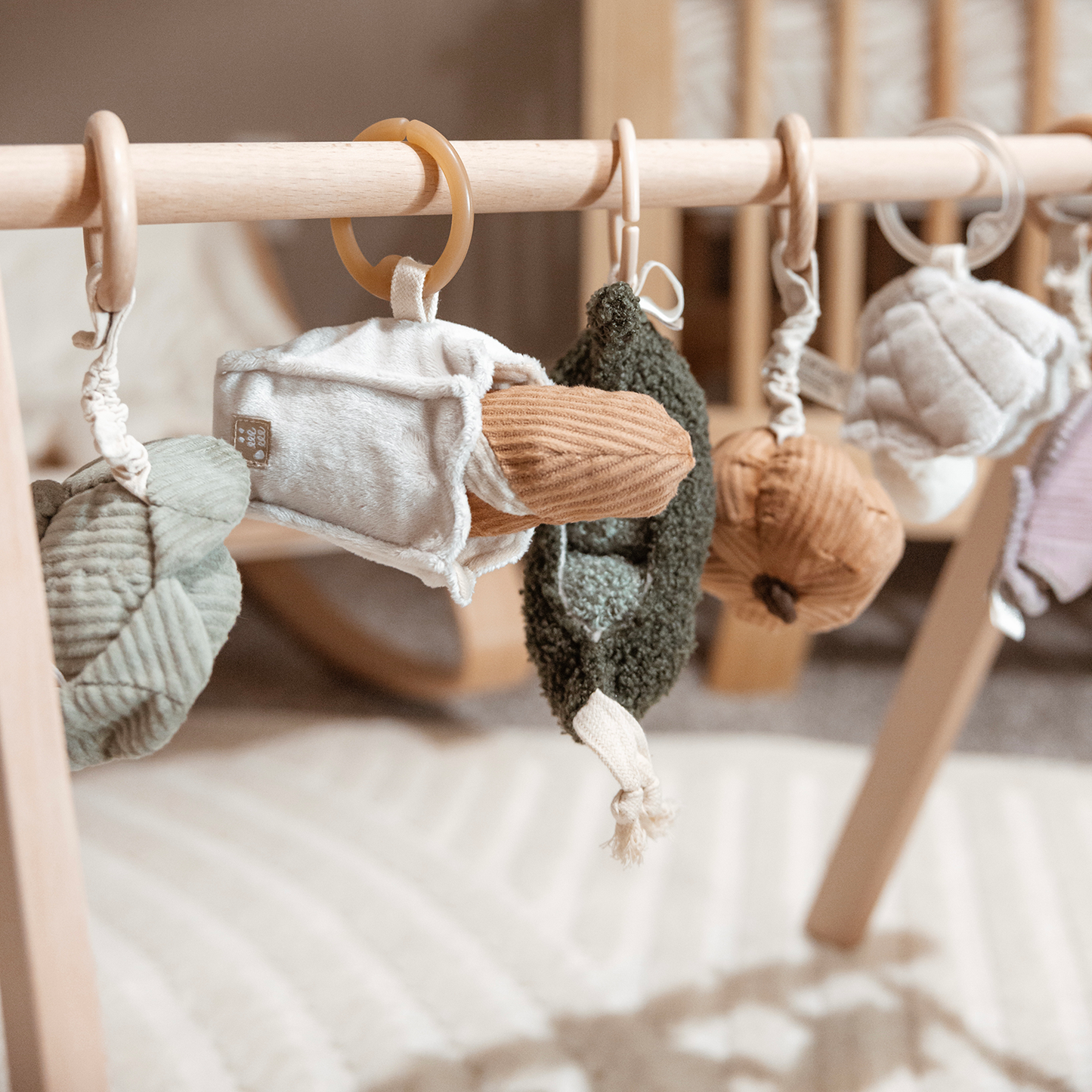 Textured baby toys hanging on a wooden crib bar with a neutral color palette.