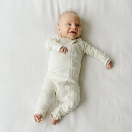 Baby wearing a white onesie lying on a white surface