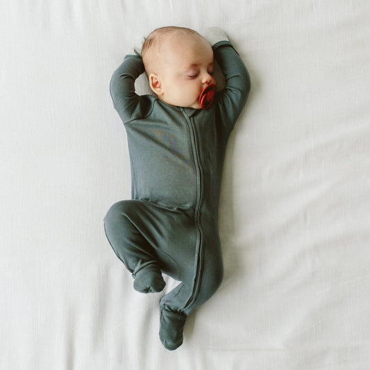 Baby in a green onesie lying on a white surface