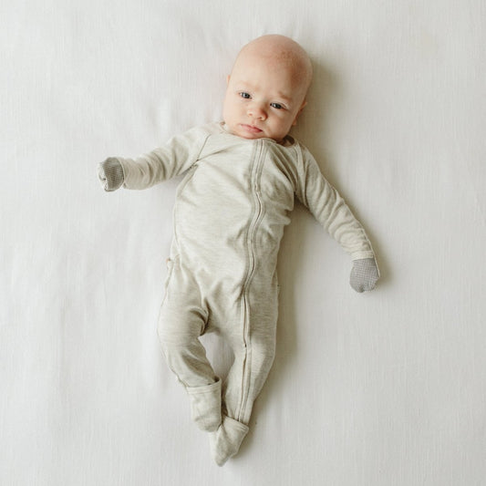 Baby wearing a light gray onesie lying on a white surface