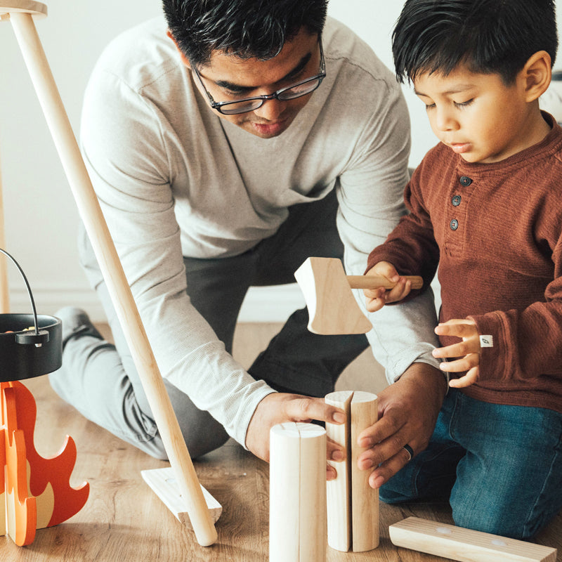 Man and child playing with wooden blocks on a wooden floor.